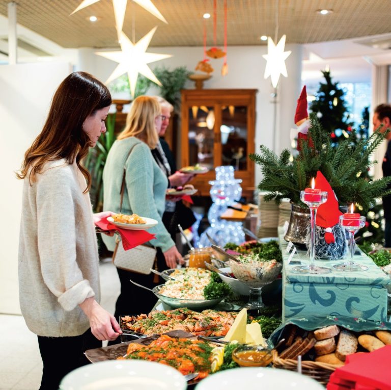 Ruokailijoita joulunoutopöydän ääressä Kymen Paviljongissa, pöydällä lohta, salaatteja ja leipää